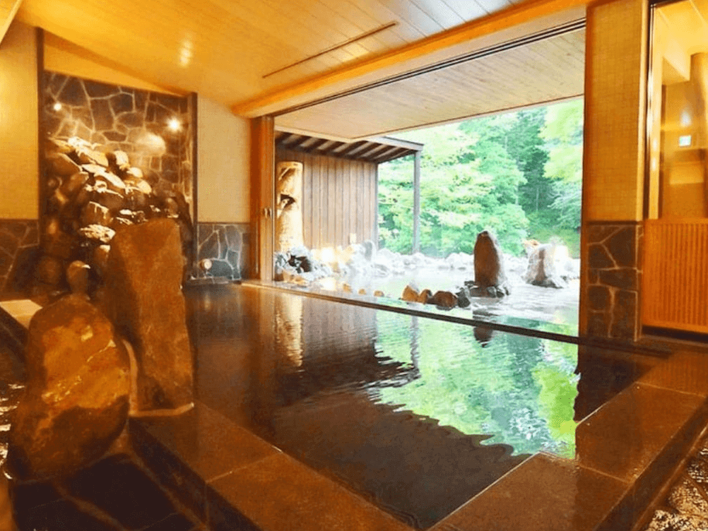 【釧路住宿】La Vista阿寒川飯店溫泉浴池，結合室內與露天設計，池畔可欣賞森林綠意與溪流景觀，營造靜謐放鬆的泡湯體驗。