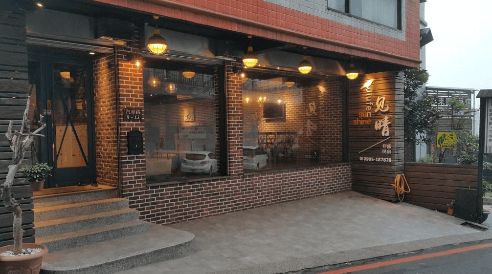 【瑞芳住宿】九份不厭晴民宿｜建築外觀夜景，紅磚立面與溫暖燈光營造溫馨氛圍，大面玻璃窗可見民宿大廳與用餐區，位於九份山城街道旁。