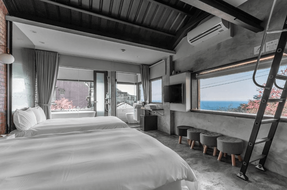 【瑞芳住宿】九份山經｜海景雙床房設有大片落地窗，可遠眺山海景色與藍天，室內以灰牆與木質家具結合現代設計，空間明亮寬敞。