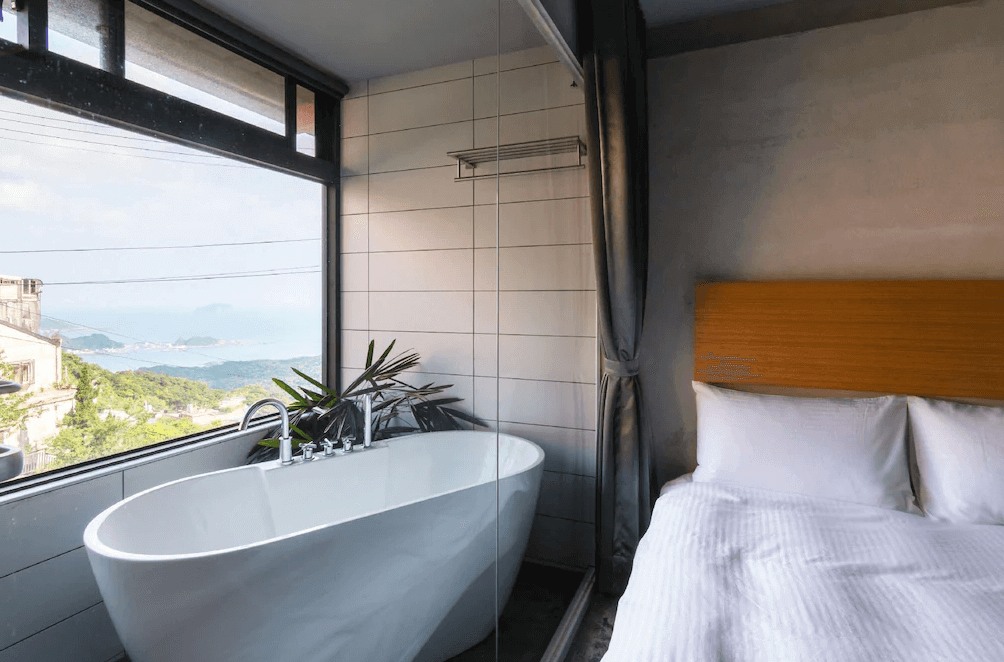 【瑞芳住宿】九份山經｜浴缸海景套房，白色浴缸設於窗邊，可邊泡澡邊欣賞九份山海景觀，房內以極簡灰白調呈現清新質感。