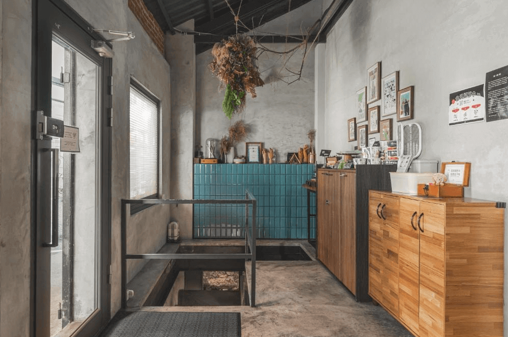 【瑞芳住宿】九份山經｜民宿接待區，灰色水泥牆搭配藍綠色磁磚與木質櫃體，牆上掛滿裝飾畫與乾燥花，展現溫馨文青氛圍。