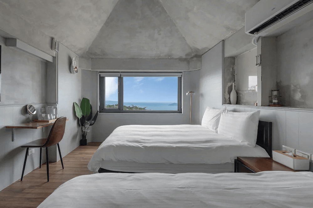 【瑞芳住宿】九份海論｜雙床海景房採極簡混凝土設計，窗外可遠眺藍色海岸線，房內以灰白色調與木質地板營造清爽舒適氛圍。
