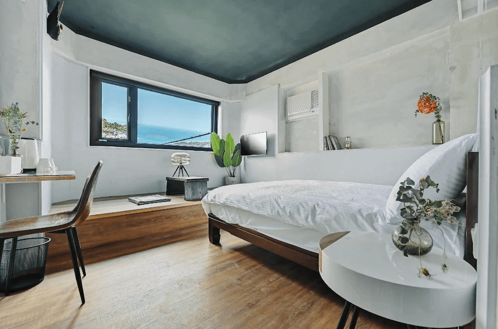 【瑞芳住宿】九份海論｜海景雙人房設計明亮，大片窗景可欣賞九份山海景，房內以白色與木質調搭配綠植點綴，展現現代簡約風格。
