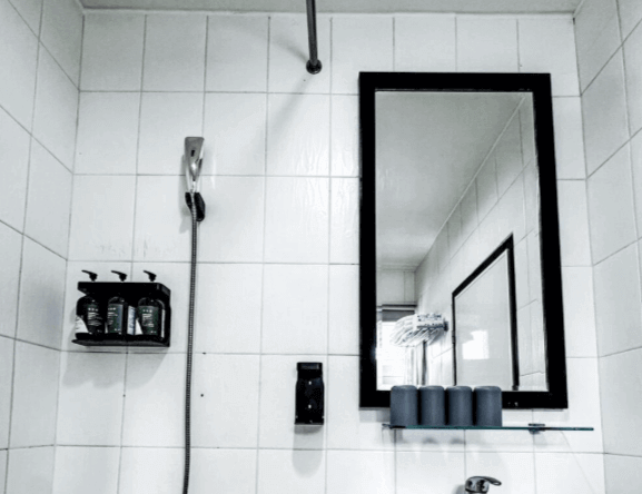 【台南寵物友善住宿】信然文旅・首學的浴室空間，採白色磁磚搭配黑框鏡面設計，配有蓮蓬頭與洗沐用品架，乾淨俐落、簡約實用。