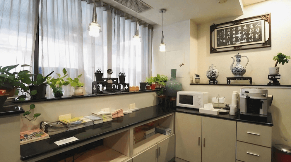 【台南寵物友善住宿】信然文旅・首學的公共空間，設有咖啡機、微波爐與閱讀資料區，搭配綠色植栽與中式書法裝飾，營造典雅舒適的休憩氛圍。