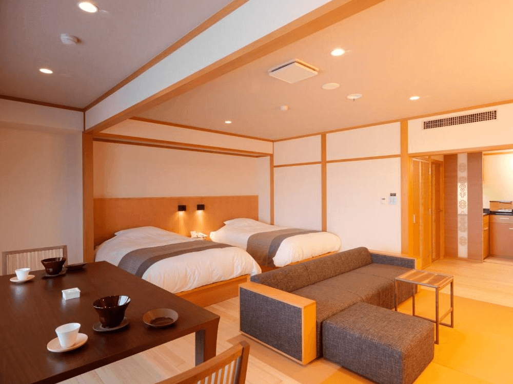 【網走住宿】「北天之丘網走湖鶴雅度假村」的現代和洋式客房，配有雙床、沙發與餐桌，整體以木質與米色調設計，空間寬敞溫馨，展現日式雅緻與現代舒適感。