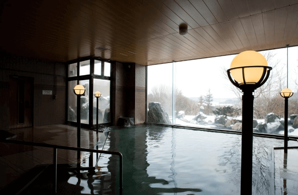 【網走住宿】「北天之丘網走湖鶴雅度假村」的室內溫泉浴場，設有大面玻璃窗可欣賞雪景，溫泉池寬敞明亮，結合自然採光與靜謐氛圍，讓旅客徹底放鬆身心。