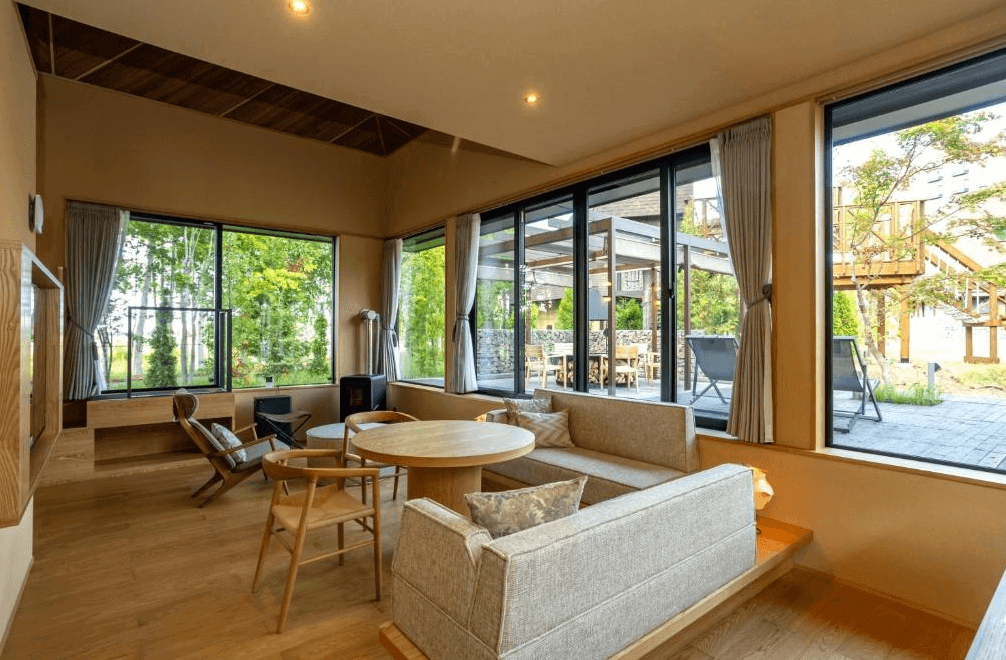 【網走住宿】「北天之丘網走湖鶴雅度假村」的大廳休憩區，以大片落地窗引入自然光線，搭配原木家具與綠意庭園景觀，營造溫暖悠閒的度假氛圍。