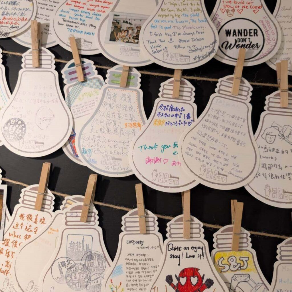 【台北背包客棧】北門臥客青年旅館留言牆展示旅客手寫的燈泡造型留言卡，寫滿各國語言的感謝與住宿心得，充滿溫馨互動感。