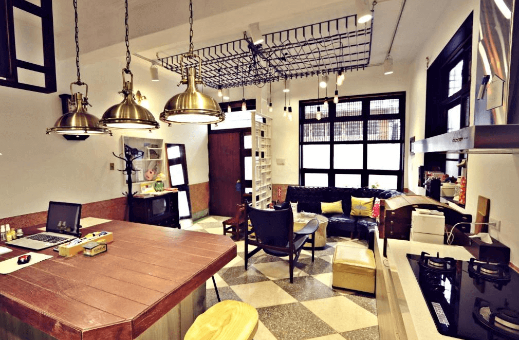 【台南寵物友善住宿】台南民宿湧福驛站的公共空間，結合廚房與客廳設計，有大型木質吧檯、復古沙發、吊燈與工業風裝飾，整體氛圍溫馨且充滿生活感，適合旅人休憩交流。