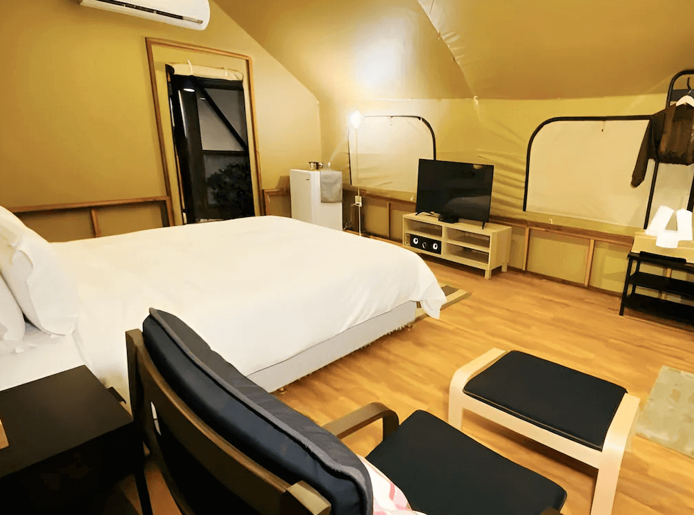 【六龜住宿】高雄六龜【國蘭花園Villa會館】豪華露營帳篷房，內部配有雙人床、電視與冷氣，木質地板與暖色燈光營造舒適氛圍，兼具自然與現代感。