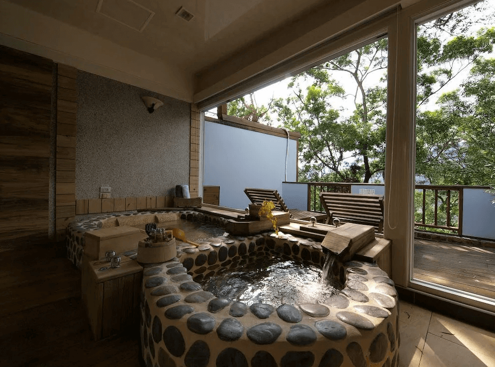 【六龜住宿】高雄六龜【國蘭花園Villa會館】室內溫泉湯屋，以鵝卵石砌成的雙人泡湯池，搭配大片落地窗可欣賞樹林景色，氛圍自然靜謐。