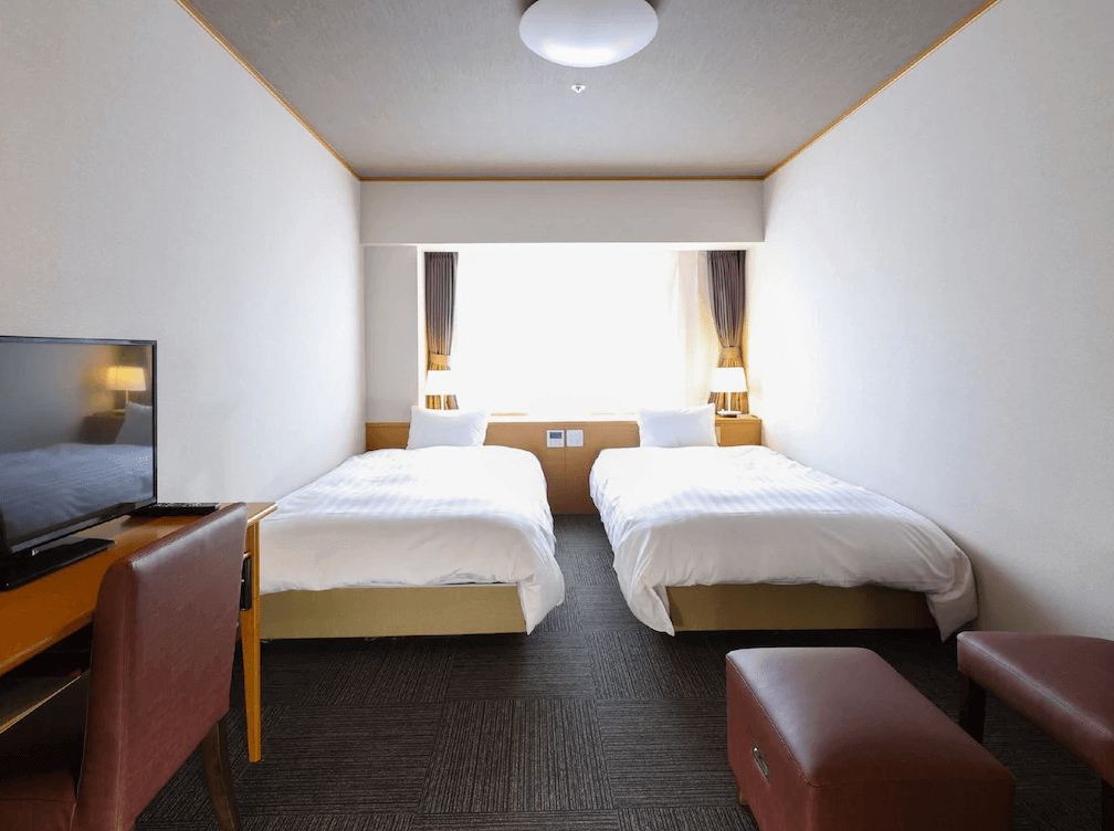 【釧路住宿】多米高級酒店－釧路天然溫泉雙床房，房間簡約明亮，配置兩張單人床、電視與書桌，窗邊自然採光良好，整體乾淨舒適。