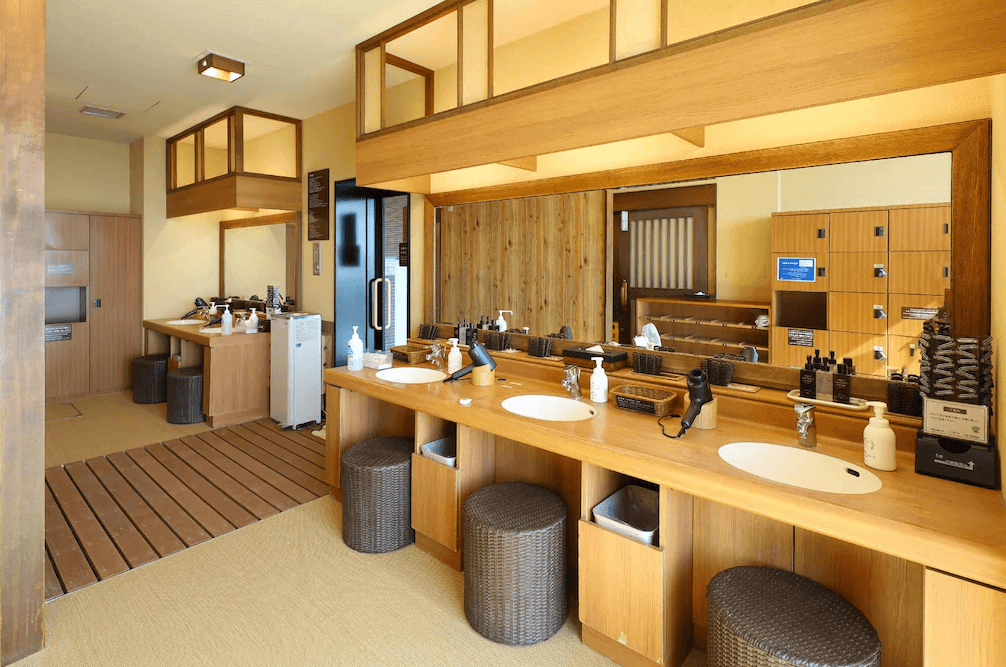 【釧路住宿】多米高級酒店－釧路天然溫泉公共盥洗與更衣區，木質設計與鏡面明亮整潔，提供洗面台、吹風機與保養用品。