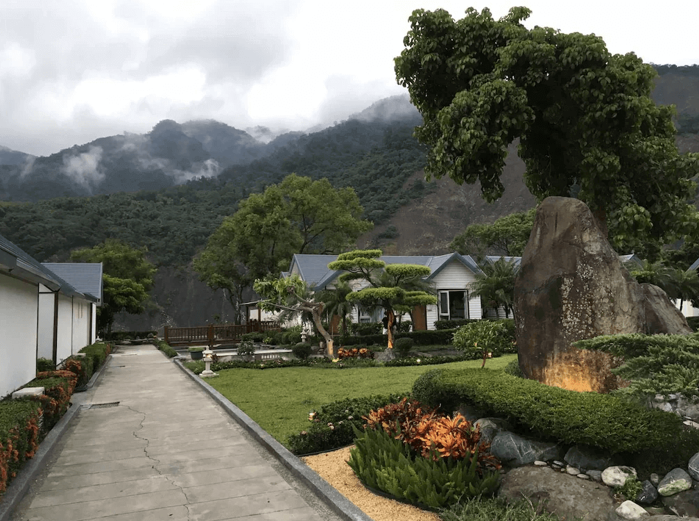 【六龜住宿】高雄六龜【寶來山澤居 Villa 渡假小木屋】園區景觀，整齊的步道與綠地庭園造景，遠處可見群山雲霧繚繞，展現自然靜謐的山林美景。