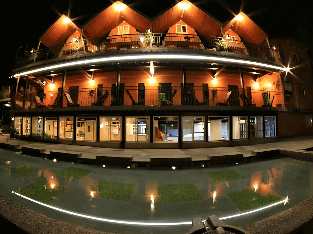 【頭城住宿】宜蘭工匠家小木屋民宿 夜間外觀，三角屋頂的木造建築倒映在水池中，燈光柔和溫暖，呈現迷人度假景緻。