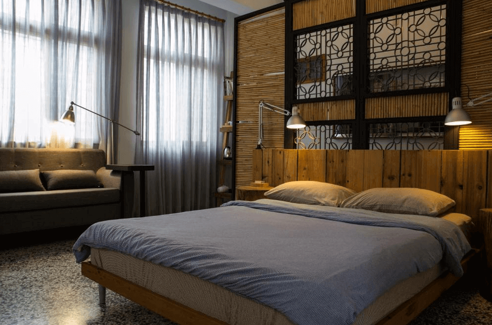 【台南寵物友善住宿】巷弄 x 台南民宿客房，以木質床架與竹編隔間設計呈現復古氛圍，大面窗簾透入柔和光線，搭配沙發與閱讀燈營造舒適質感。