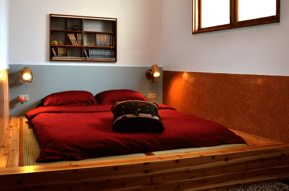 【台南寵物友善住宿】巷弄 x 台南民宿和式臥室，紅色床鋪搭配木質地板與壁燈設計，牆上設有懸掛書架，整體展現溫馨的日式居家風格。
