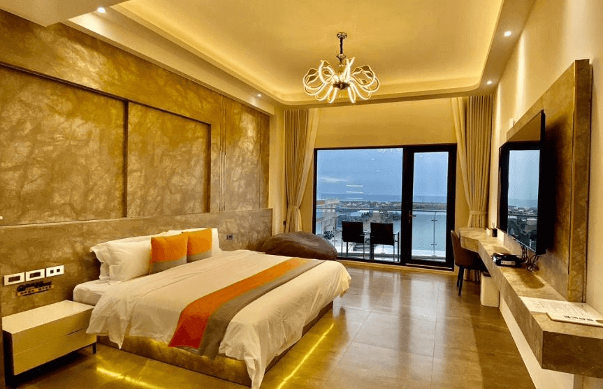 【枋寮住宿】「愛琴海岸海景精品民宿的海景雙人房，金色燈光營造溫馨氛圍，設有陽台可遠眺港景與夕陽，房內配備大螢幕電視與舒適大床。」