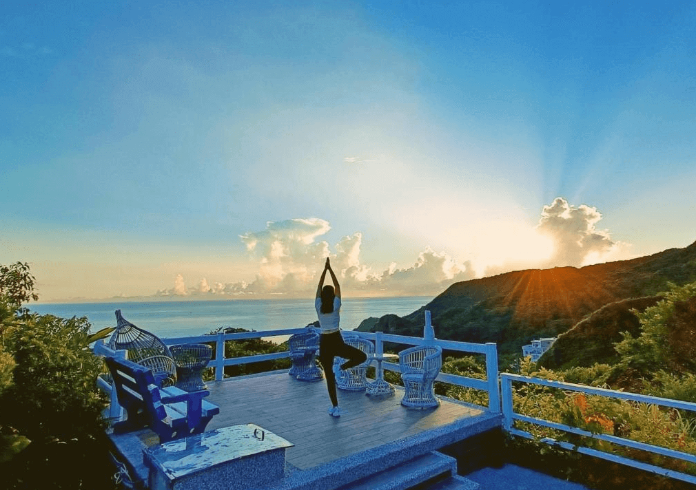 【瑞芳住宿】應許美地民宿｜旅客在戶外觀景平台做瑜伽迎接日出，前方是遼闊的太平洋與山海景色，晨光灑落充滿寧靜氛圍。