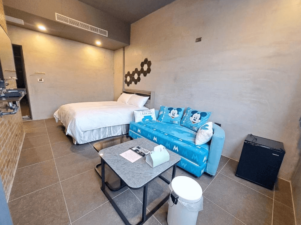 【枋寮住宿】「春枋旅居 雙人房，牆面為水泥灰色調，房內配有藍色米奇圖案沙發與茶几，整體風格現代簡約、溫馨明亮。」