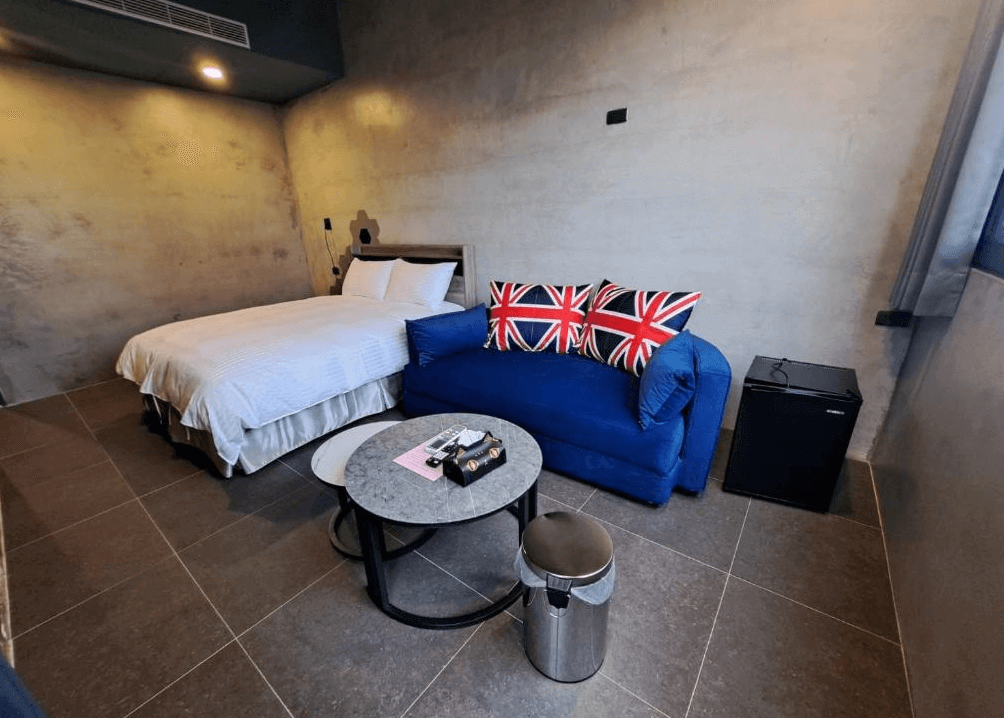 【枋寮住宿】「春枋旅居 雙人房一景，搭配深藍英國旗抱枕沙發與小圓桌，牆面水泥質感設計，呈現工業風格。」