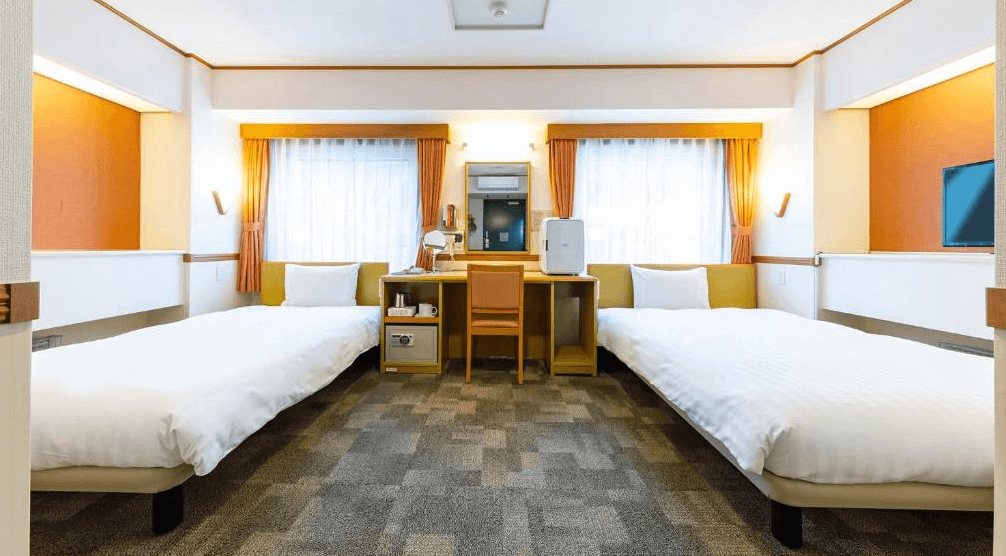 【網走住宿】「東橫INN北海道鄂霍次克網走站前」的雙床房，設有兩張單人床與中央書桌，房間以橘色與米色調設計，採光明亮、空間整潔舒適。