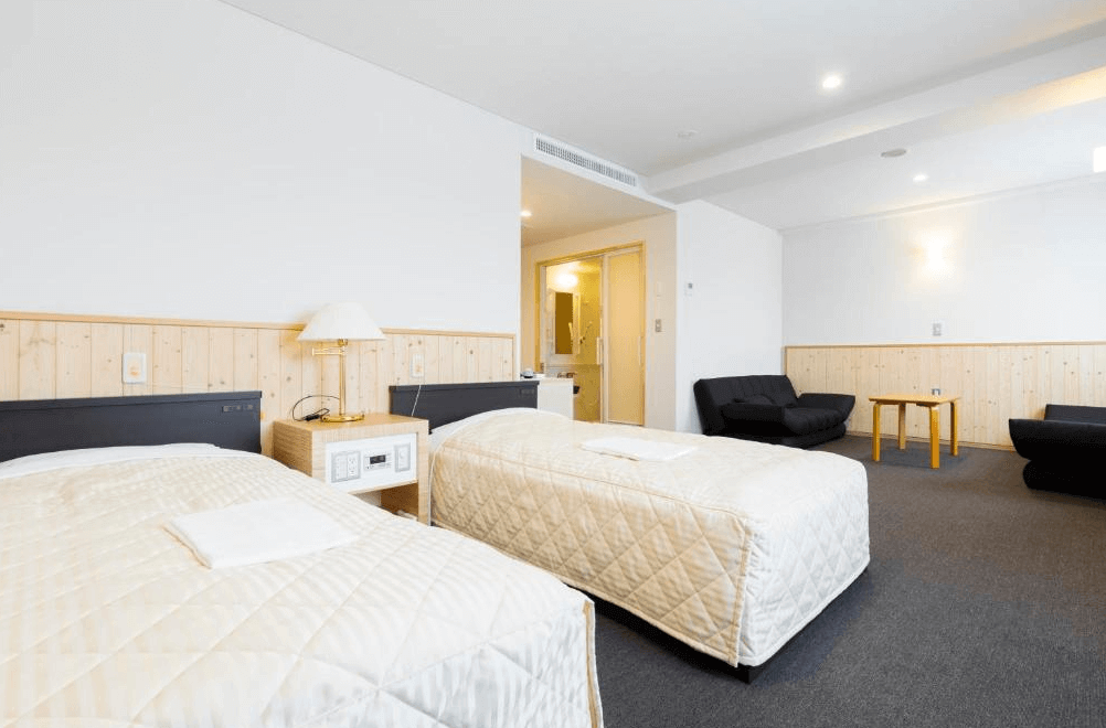 【網走住宿】「東藻琴村酒店」的雙床客房，採用溫潤木質牆面設計與簡約白色調，空間寬敞明亮，設有沙發與小茶几，展現舒適的北歐風格住宿氛圍。