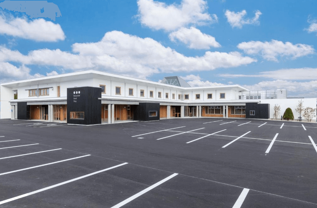 【網走住宿】「東藻琴村酒店」的外觀全景，白色與黑色調搭配木質元素的現代建築風格，前方設有寬闊停車場與晴朗藍天下的清新景致。