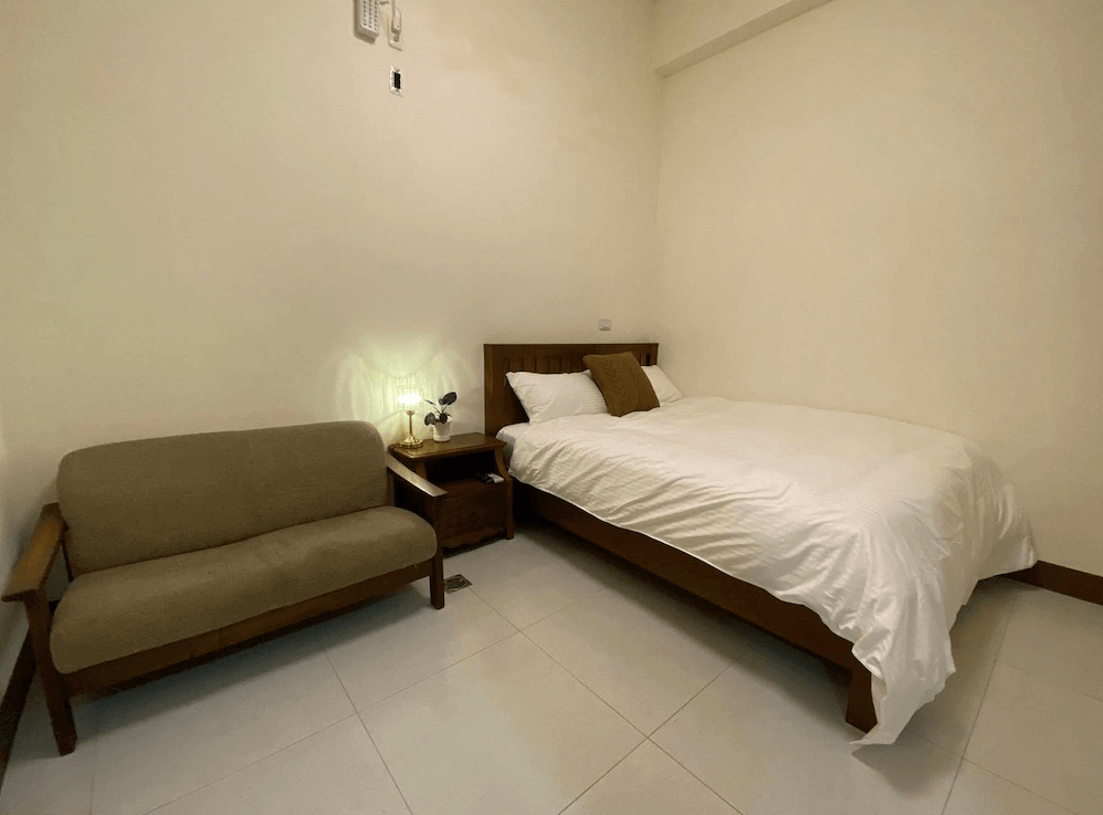 【枋寮住宿】「枋寮18遛遛居 雙人房，木質家具搭配簡約米色調設計，房內設有小沙發與床頭燈，營造溫馨舒適氛圍。」