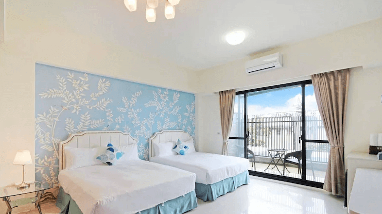 【枋寮住宿】「枋寮帝寶16民宿 四人房，牆面採藍色花卉設計，兩張雙人床整潔明亮，落地窗外為陽台空間，可享受自然光線與遼闊視野。」