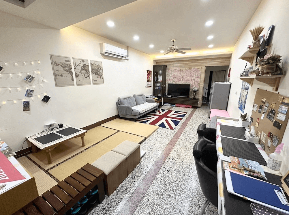 【枋寮住宿】「枋寮枋居背包客棧 公共交誼廳，設有榻榻米區、沙發、電視與桌椅，牆面佈置旅遊照片與地圖，氛圍溫馨舒適。」