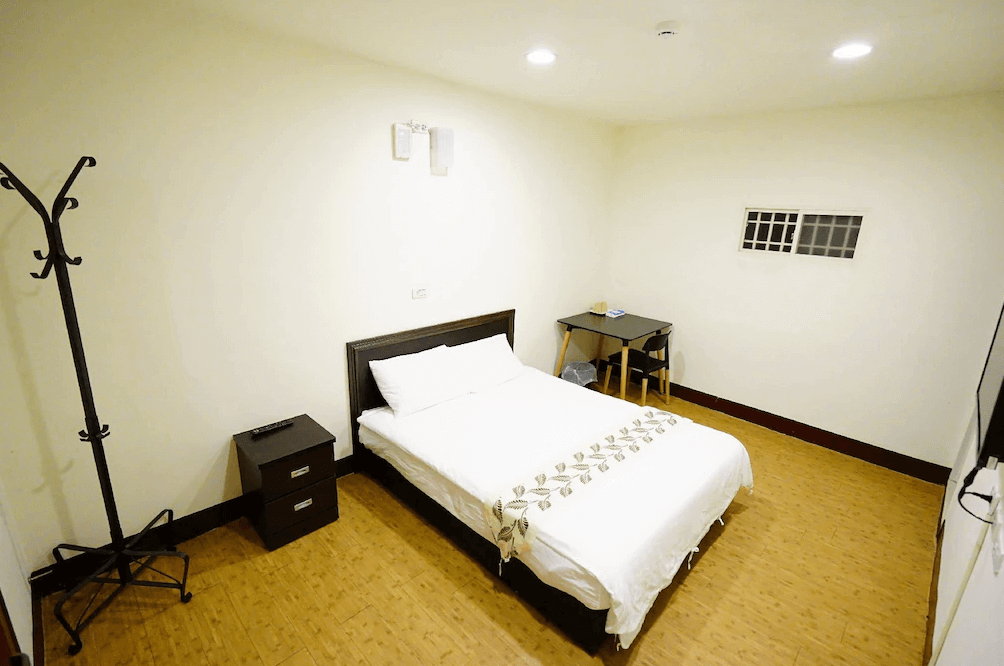 【瑞芳住宿】清芳民宿房型一覽，簡約明亮的雙人房設計，配有雙人床、書桌、吊衣架與床邊櫃，空間寬敞整潔，地板採木質紋理設計，營造舒適住宿氛圍。