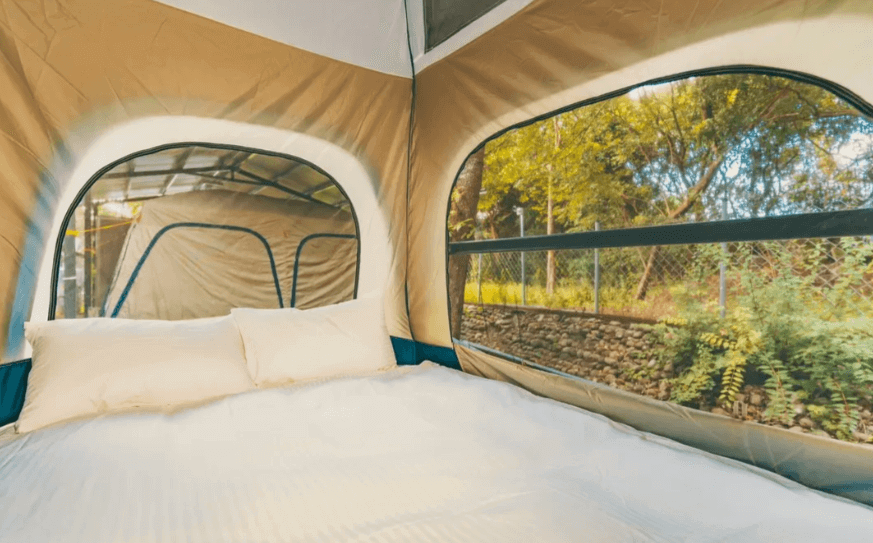 【六龜住宿】高雄六龜【溫德莊園】帳篷內部臥鋪，白色床鋪搭配大型窗景，能欣賞戶外樹林景色，氛圍自然悠閒。