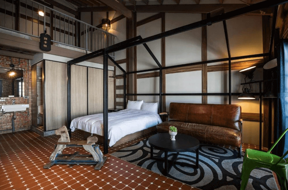 【台南寵物友善住宿】玩聚安平民宿的樓中樓客房，結合工業風與復古元素設計，紅磚牆、皮沙發與木質結構打造溫暖氛圍，房內設有雙人床與開放式衛浴空間。