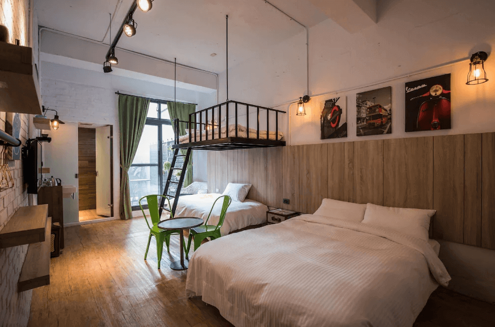 【台南寵物友善住宿】玩聚安平民宿的四人房，以木質牆面與吊燈設計營造溫馨氣氛，設有上下層床位與大片落地窗，空間明亮寬敞，充滿工業風格。