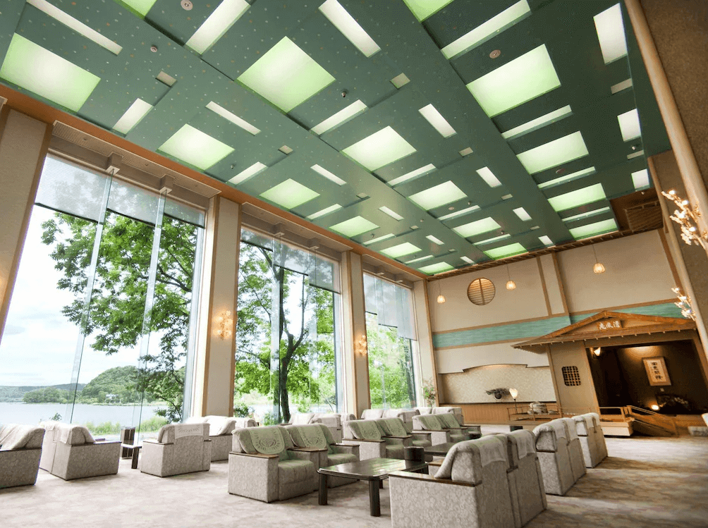 【網走住宿】「網走湖莊大飯店」的大廳休憩區，挑高設計搭配綠意窗景與柔光照明，設有舒適沙發與湖景觀景窗，展現典雅的日式飯店格調。