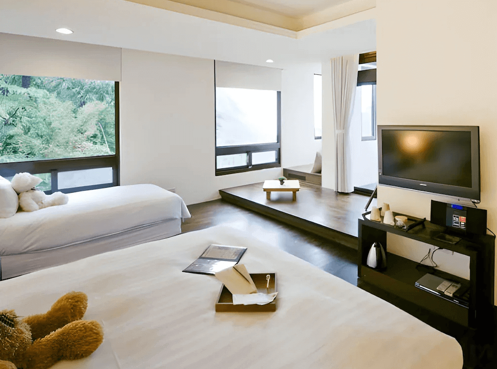 【瑞芳住宿】緩慢民宿 金瓜石｜溫馨雙床房，大片窗景迎入山林綠意，房內以白色與原木色調為主，設有電視與閱讀區，呈現寧靜自然的住宿氛圍。