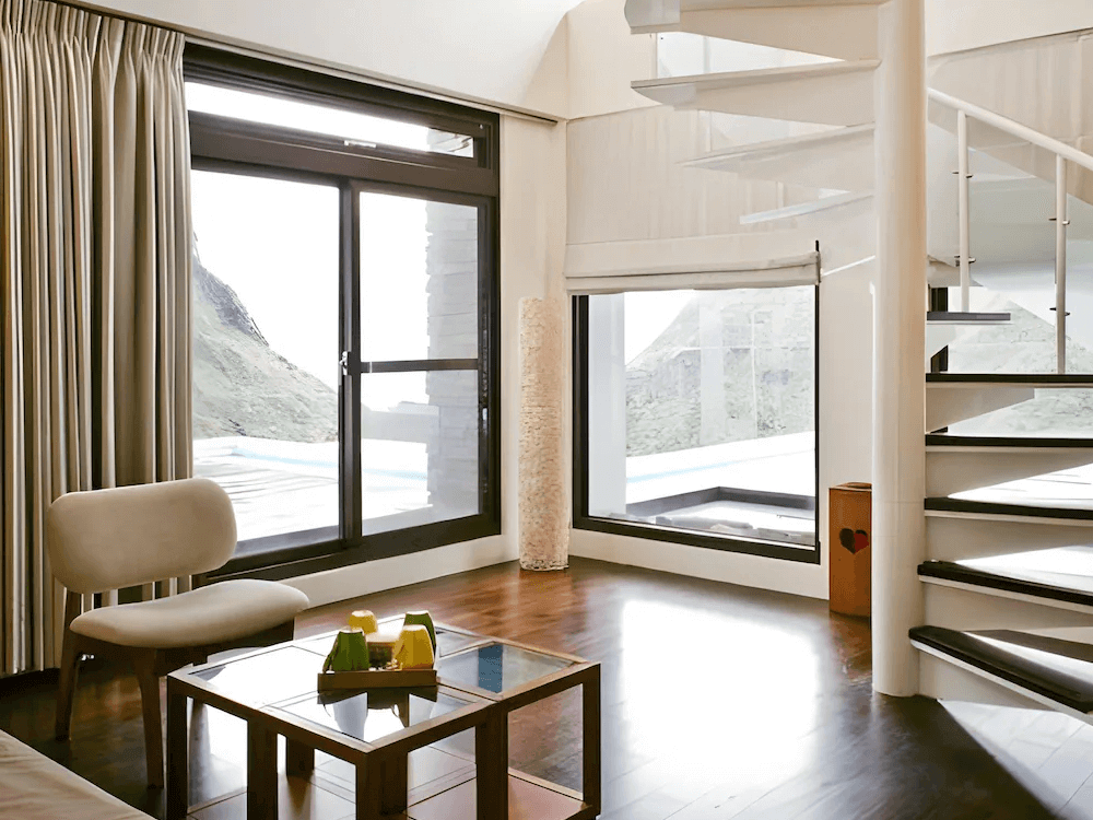 【瑞芳住宿】緩慢民宿 金瓜石｜房內挑高採光設計，大片落地窗可眺望山景與海景，螺旋階梯通往閣樓，空間明亮充滿設計感。