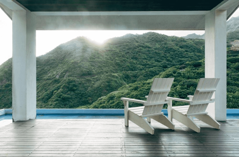 【瑞芳住宿】緩慢民宿 金瓜石｜露台景觀區設有兩張白色木椅，可遠眺翠綠山巒與夕陽光影，是放鬆休憩與賞景的絕佳位置。