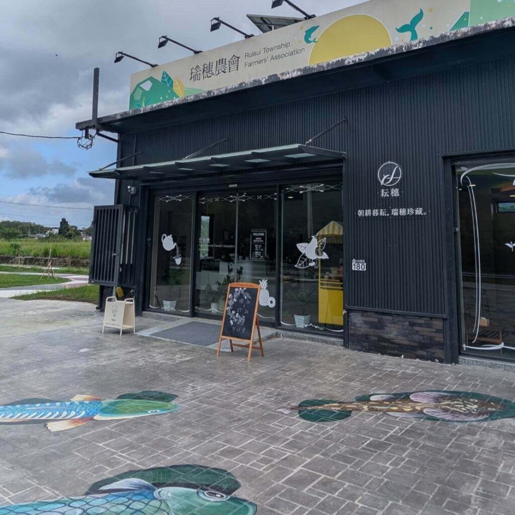 【瑞穗美食】「縱谷耘穗咖啡廳」外觀，建築外牆為黑色工業風設計，招牌上標示「琍穗農會」，前方地面彩繪有魚群圖案，入口擺放木製黑板菜單，整體環境乾淨寬敞，鄰近綠意田野。