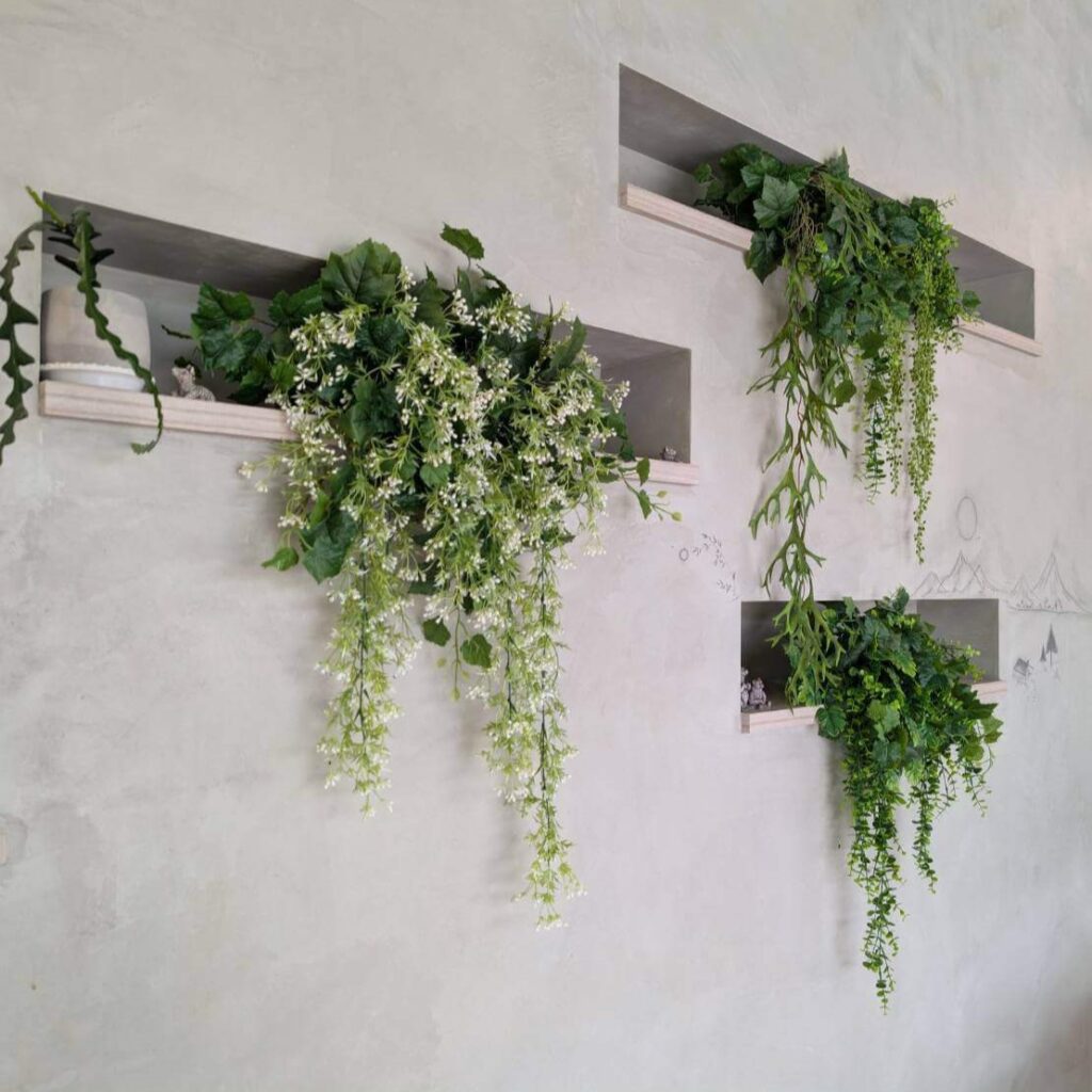 【瑞穗美食】「縱谷耘穗咖啡廳」內部牆面裝飾，牆上嵌入層架擺放綠色植物與垂墜花卉，背景為簡約灰白牆面，整體風格自然清新，營造舒適放鬆的氛圍。