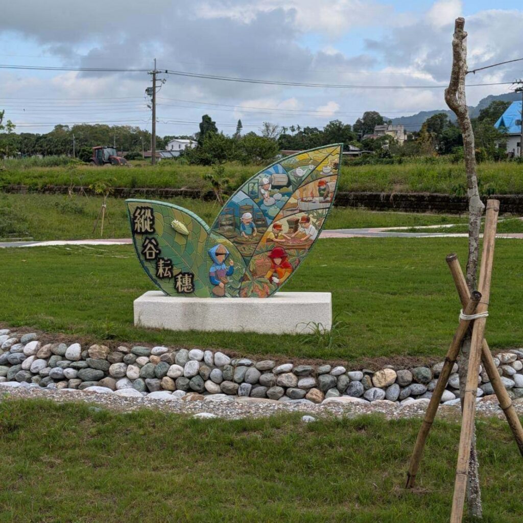 【瑞穗美食】「縱谷耘穗咖啡廳」戶外庭院的裝置藝術，以兩片綠色葉片造型的馬賽克拼貼雕塑呈現，圖案描繪農民與地方產業意象，象徵農村文化與自然共生，周圍綠草如茵，景致悠閒。