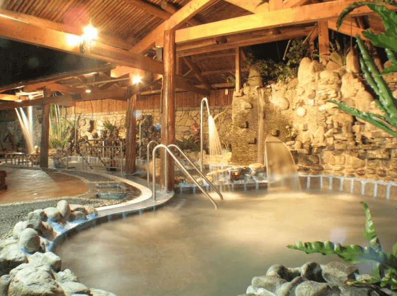 【六龜住宿】高雄六龜【美崙山溫泉渡假山莊】露天溫泉池夜景，木造屋頂與石砌池邊搭配燈光映照，溫泉水霧繚繞，氛圍悠閒浪漫。