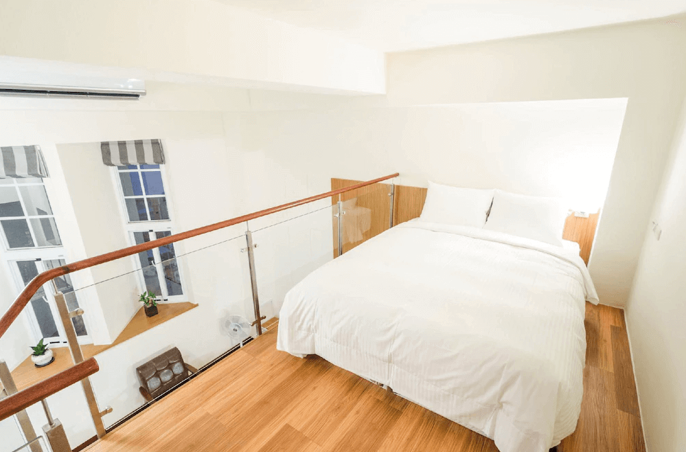 【台南寵物友善住宿】肯辛頓旅店樓中樓雙人房，採用溫潤木質地板與純白床鋪設計，透過玻璃欄杆與大面窗戶引入自然光線，營造明亮舒適的休憩空間。