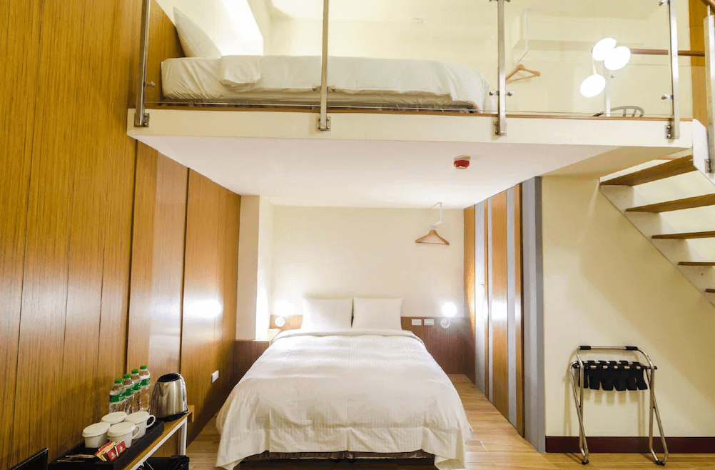 【台南寵物友善住宿】肯辛頓旅店樓中樓房型，下層設有雙人床與簡約木質牆面，上層為挑高閣樓床鋪，空間設計現代俐落，展現高質感旅宿氛圍。