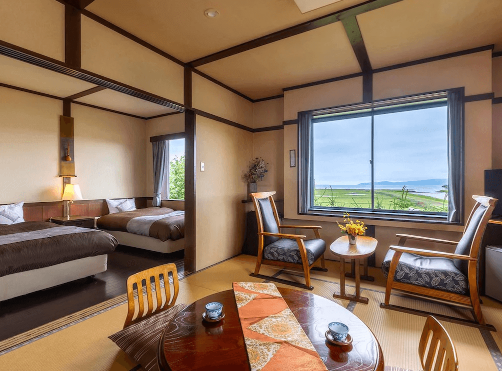 【網走住宿】"網走住宿精選示意圖"「能取之莊 Kagari 屋」的和洋式客房，榻榻米空間搭配木質家具與低矮茶几，窗外可遠眺能取湖與遼闊草原景色，氛圍溫馨雅緻。