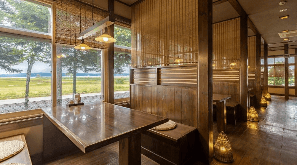 【網走住宿】「能取之莊 Kagari 屋」的餐廳空間，以木質隔間與竹簾營造私密感，大片落地窗可欣賞能取湖畔綠意景致，呈現自然與和風融合的用餐環境。