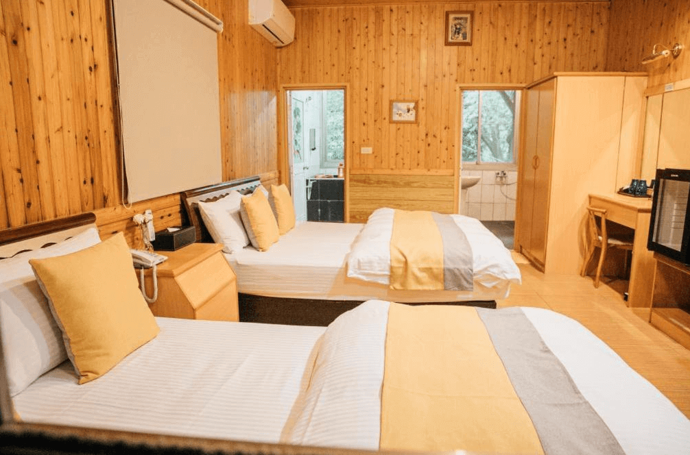 【六龜住宿】高雄六龜【草地人Spa民宿】雙床家庭房，整體以溫潤木質調設計，搭配黃白相間床巾與柔和燈光，空間明亮溫馨，附書桌與衣櫃，適合家庭入住。