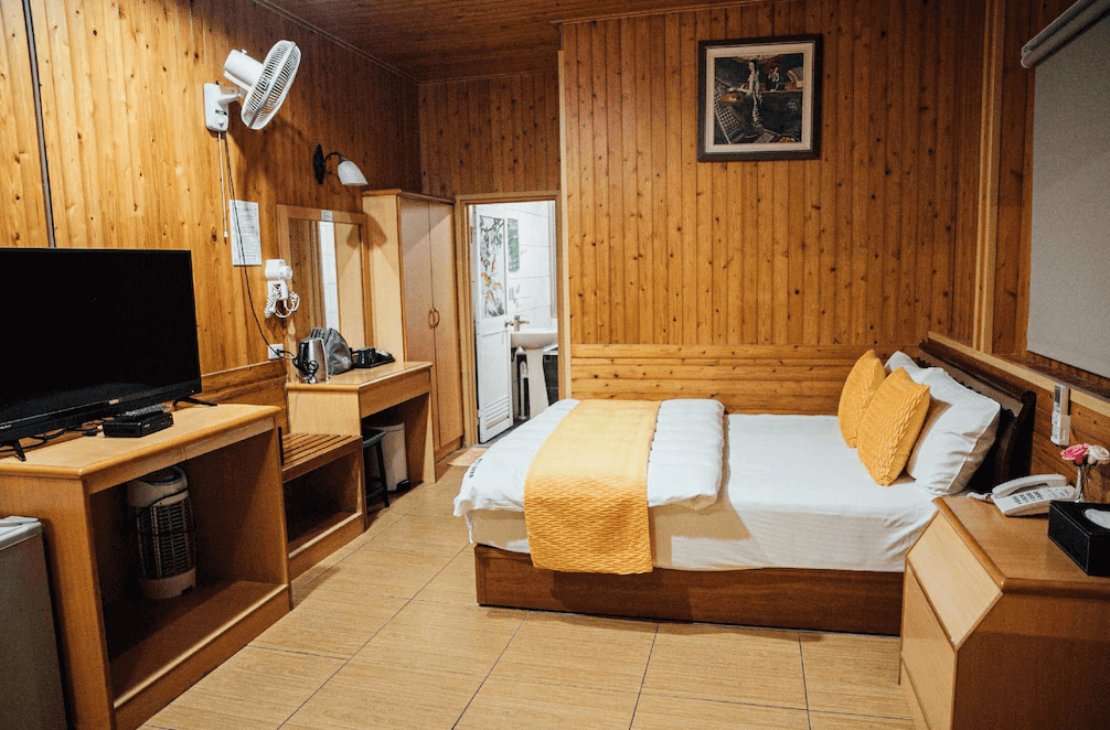 【六龜住宿】高雄六龜【草地人Spa民宿】雙人房，木質牆面與家具營造自然溫暖氛圍，配有電視、梳妝台與茶具設備，整體乾淨整潔且具舒適感。